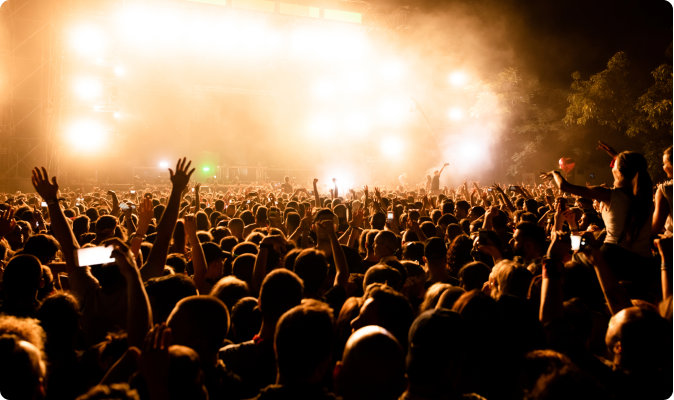 Large crowd at a concert with bright stage lights and smoke.