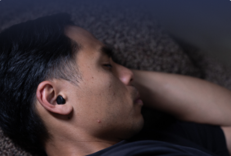 Man wearing a black earbud lying on a textured surface