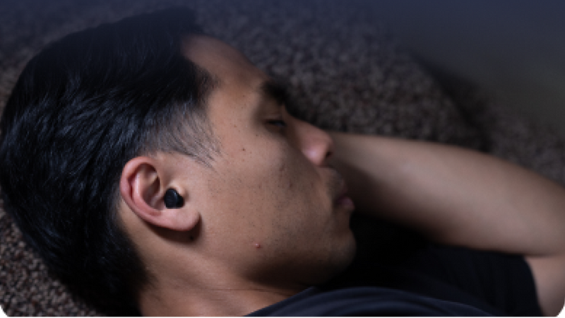 Person wearing earplugs lying on a textured surface